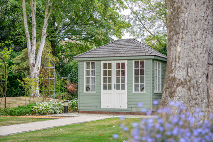 Cley Summerhouse A small sage green summerhouse with traditional weatherboard cladding and contrasting white window frames and door